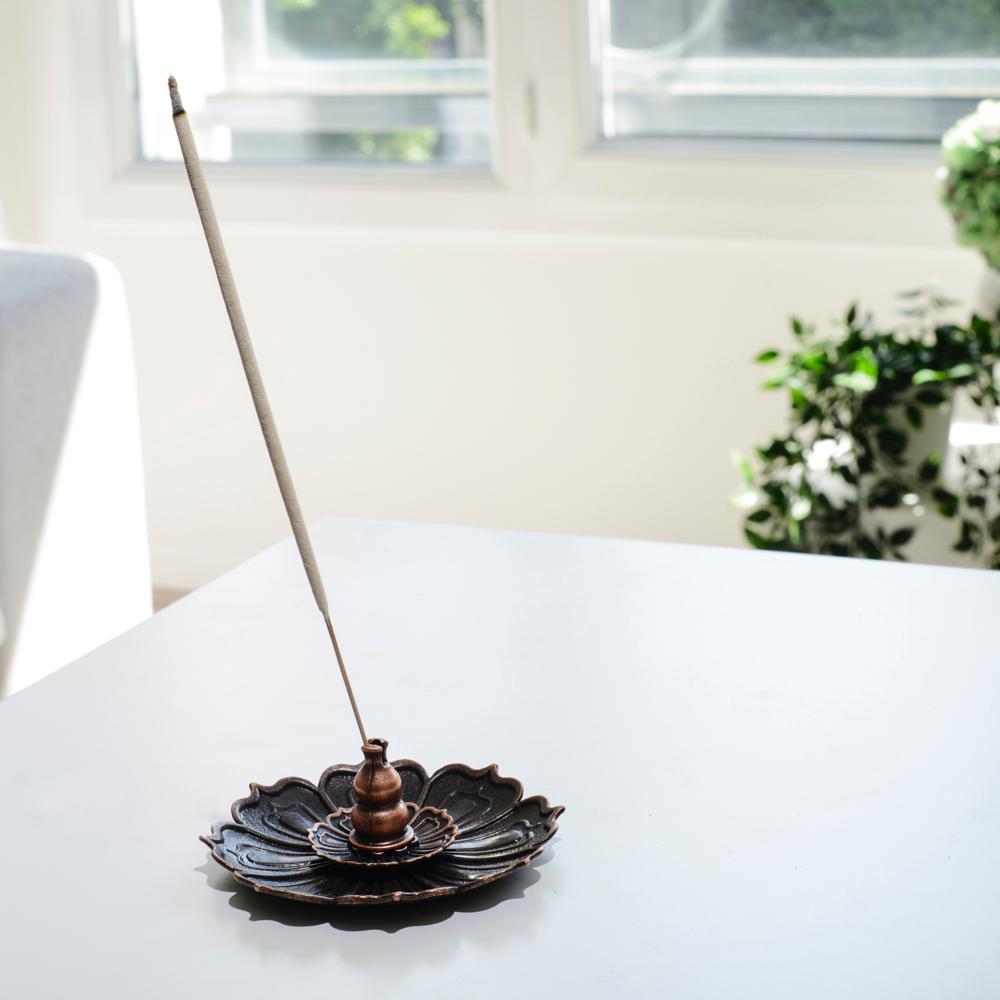 Porte encens bohème en forme de lotus de bronze posé sur une table dans un salon à l’ambiance cocooning