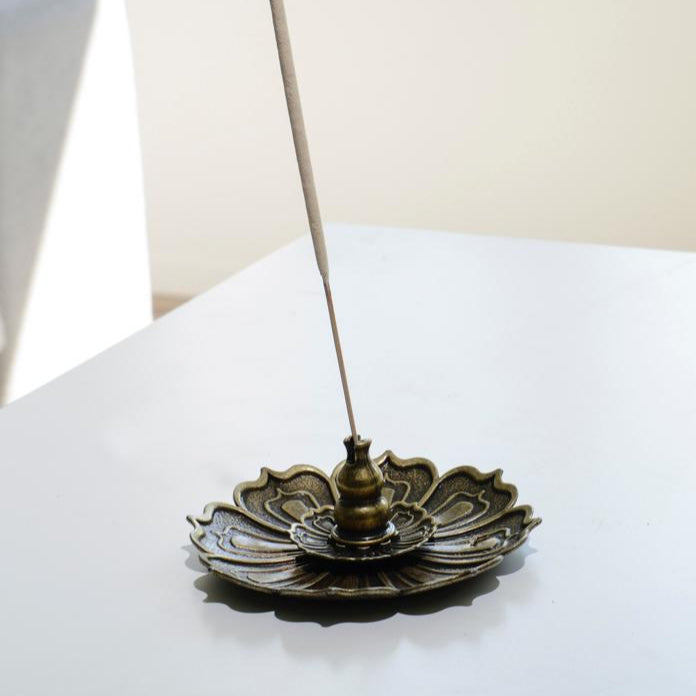 Porte encens bohème en forme de lotus de bronze posé sur une table dans un salon à l’ambiance cocooning